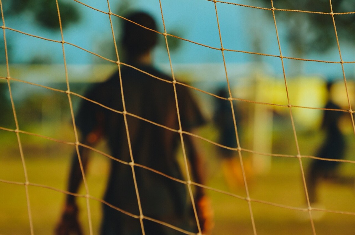 A goalkeeper seen from behind through the goal net, waiting for play