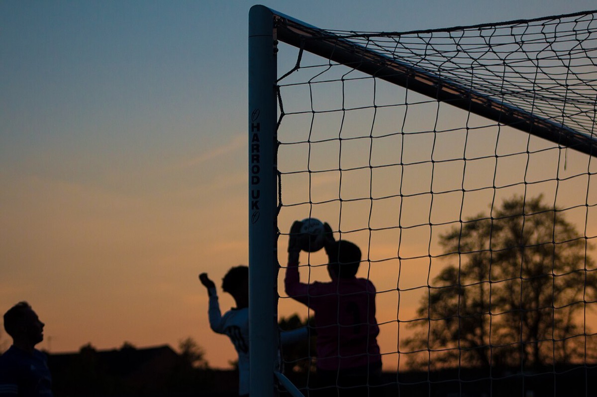 Silhouette of a goalkeeper catching a high ball in front of the net at sunset